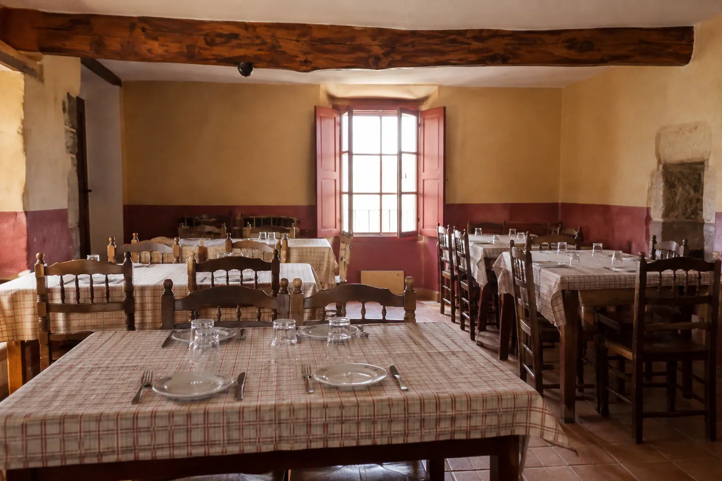 Comedor de un mesón con las mesas puestas y las sillas de madera, antes del servicio
