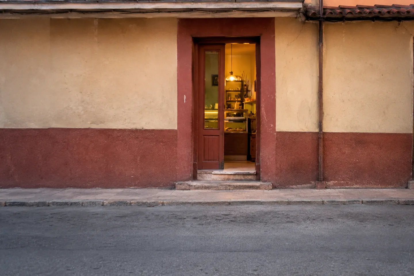 Puerta de un local abierto vista desde la acera de enfrente, con el interior iluminado al atardecer